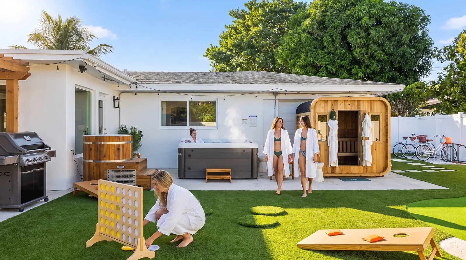 Guests in robes walking from the cedar sauna past the hot tub and cold plunge in the backyard of the lynxresort West Palm Beach house