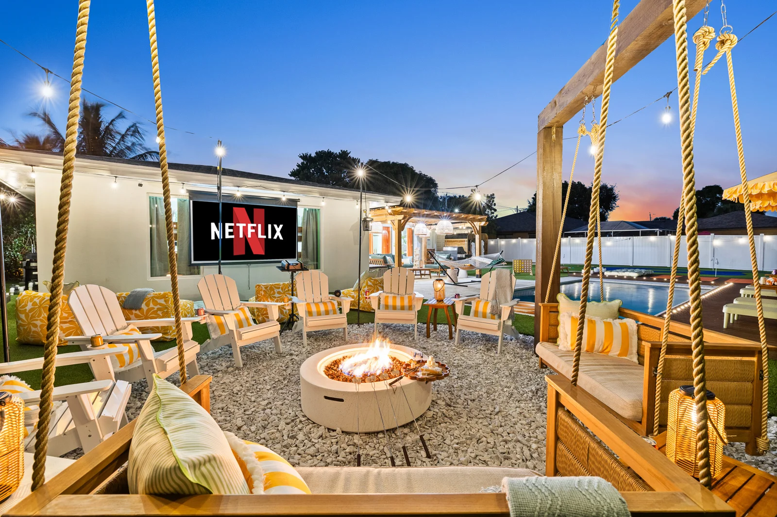 Fire pit lounge with swing seating and the outdoor movie screen at dusk